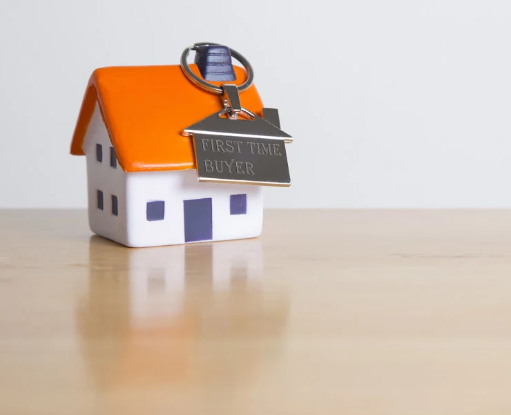 A small ceramic house with an orange roof and a keychain attached to it that reads 'FIRST TIME BUYER'.