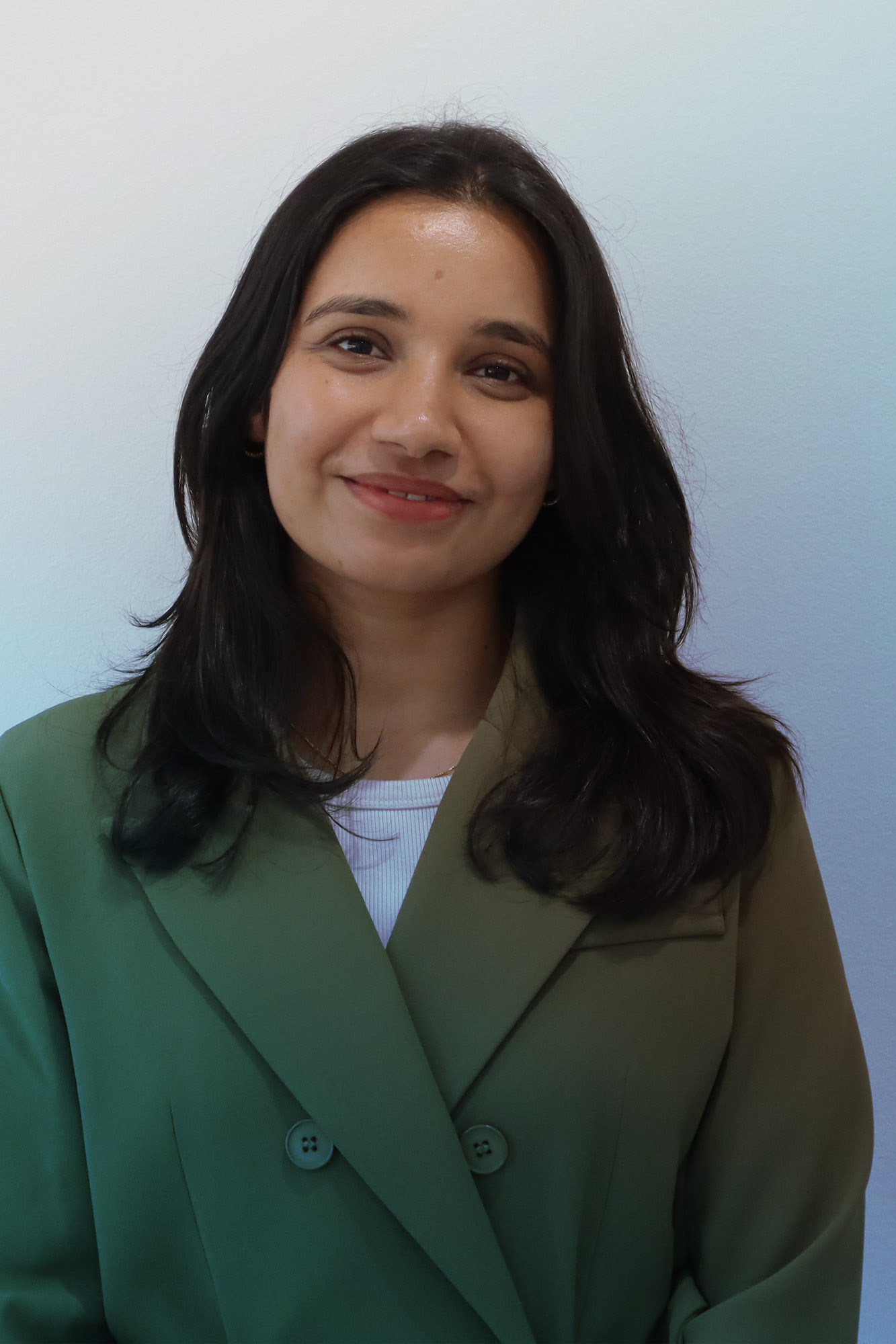 Portrait of a woman with long dark hair wearing a green blazer, smiling slightly.