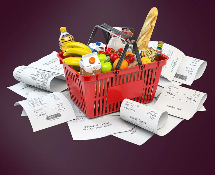 A red shopping basket filled with various groceries, surrounded by scattered receipts.