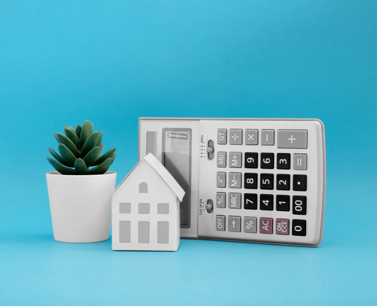 Small house model with a calculator and a potted plant on a blue background.