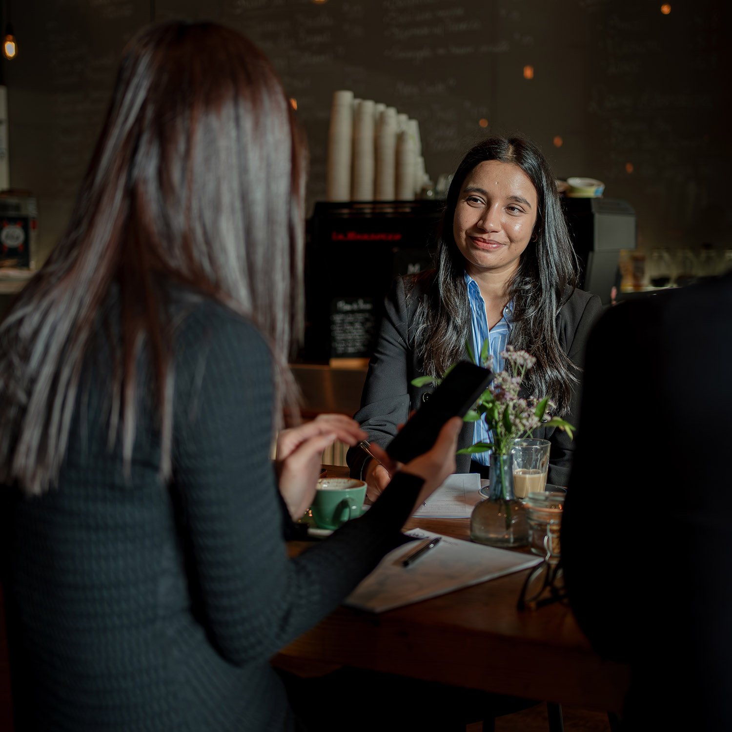 Pratistha Khatiwada, the Operations Manager at ActOn Wealth, engaging with a client at a casual business meeting in a café setting, demonstrating attentive customer interaction with a pleasant expression.