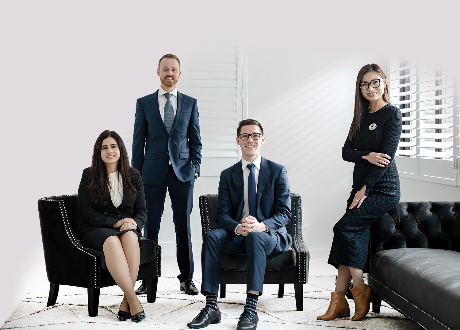 Team photo of ActOn Wealth at their office, featuring four professionals smiling. From left to right, there's a woman and three men, dressed in business attire, two seated and two standing, in a modern office setting with a bright backdrop and stylish furniture.