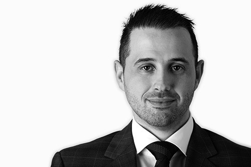 Black and white headshot of Alex Bernshteyn, Director of Actonwealth, dressed in a formal suit and tie, smiling confidently.