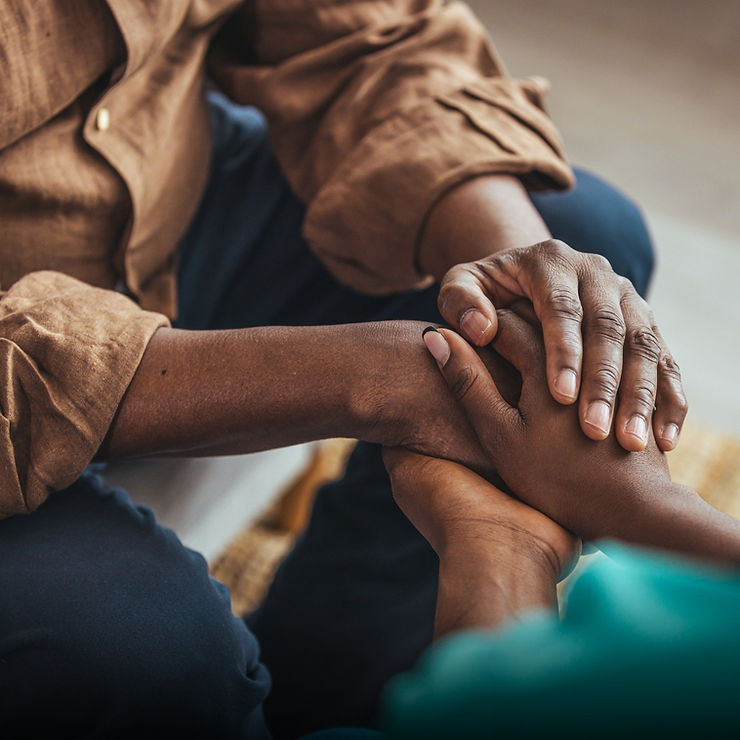 Two people holding hands in a comforting gesture, with a close-up focus on their hands.